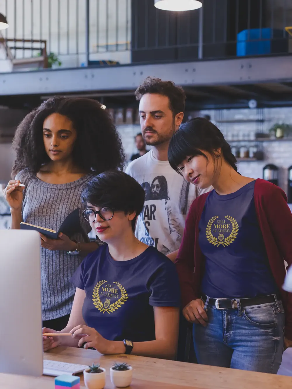 Team wearing navy Sell More Academy t-shirts reviewing work together at a desk